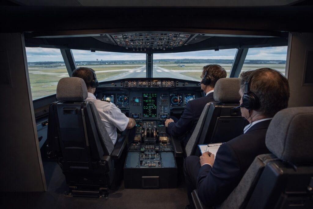 Simulation d’évaluation finale APS-MCC dans un simulateur de vol : deux pilotes en cockpit et un examinateur observant depuis le siège arrière lors d’un scénario LOFT.